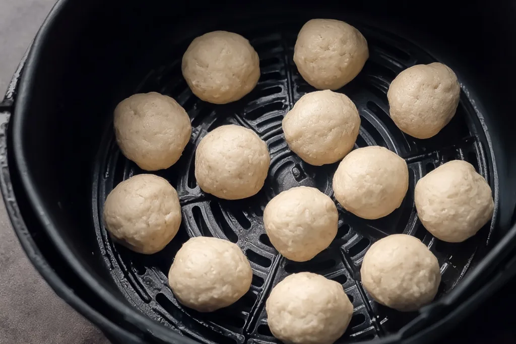Raw protein donut hole dough arranged in air fryer basket before cooking