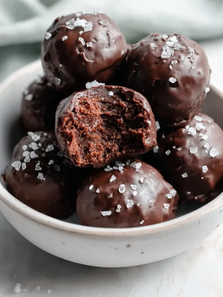 High-Protein Brownie Balls — No-Bake, Low Sugar 7 chocolate high-protein brownie balls with sea salt flakes and one bitten open