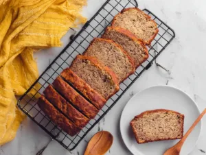 Sliced flourless banana bread on cooling rack with one slice on plate