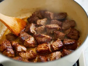 Hearty 30-Minute Vegetable Beef Soup 16 Browning beef cubes in a white Dutch oven with a wooden spoon