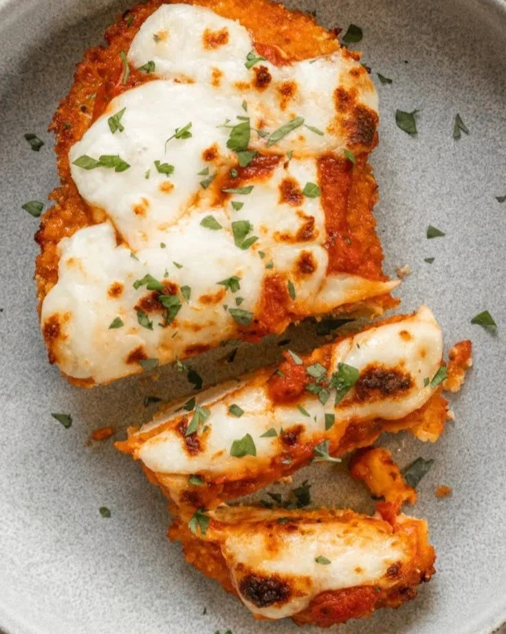 Delicious Chicken Parmesan served with pasta and fresh herbs on a white plate.